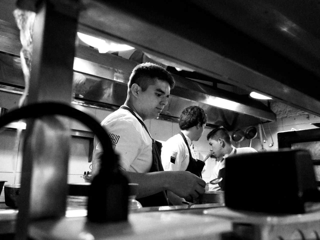 Black and white candid shot of chefs working in a high-pressure environment, reflecting the complex reality of a toxic kitchen culture and the labor behind the industry.
